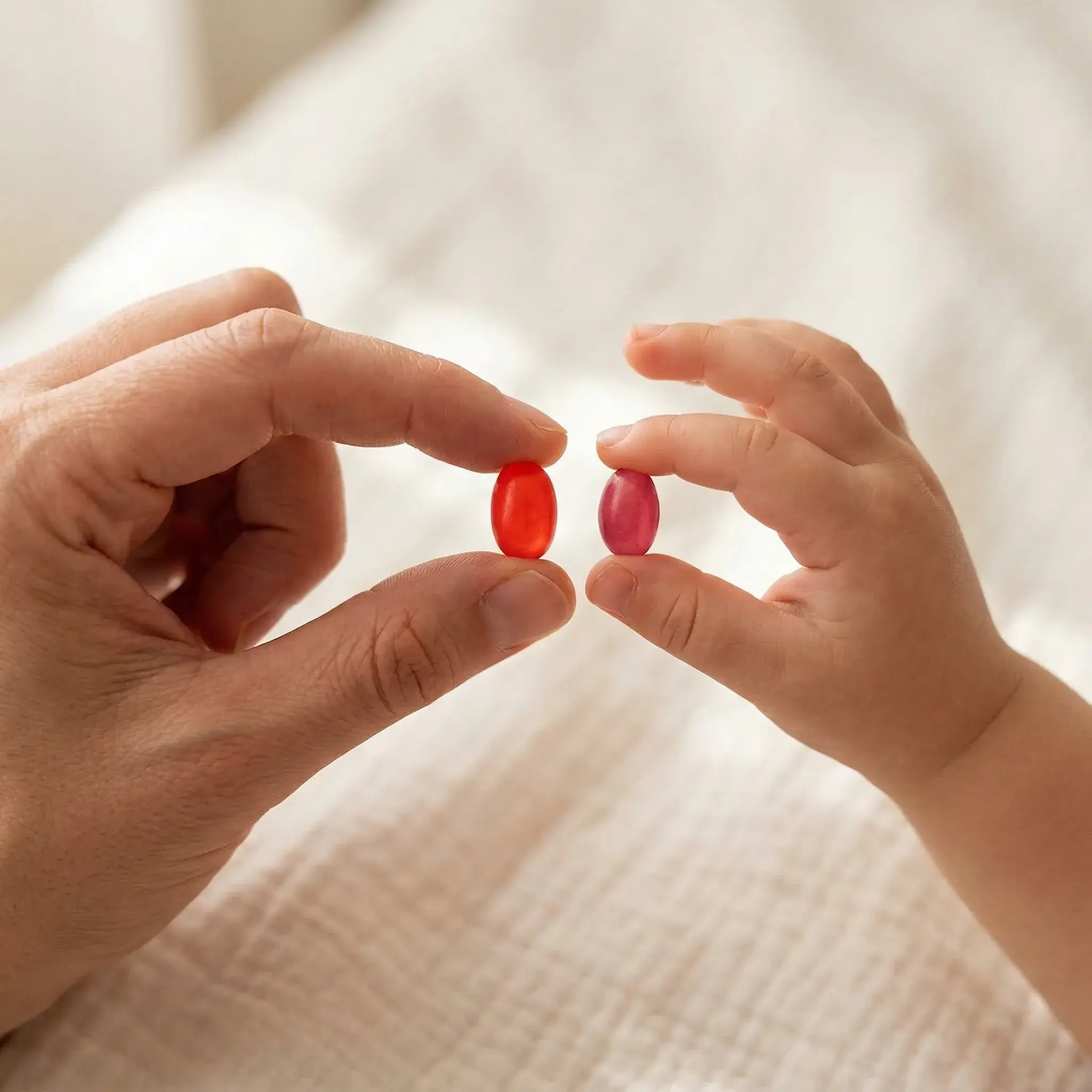 Adult and child hands holding red and pink Human Beanz jelly bean gummy supplements together